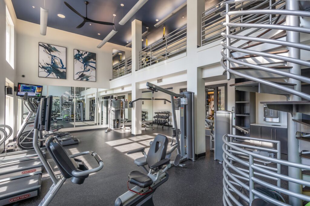 A massive 2 story gym with plenty of gym equipment including machines, weights, TVs, screens on the machines, and presumably more out of view.