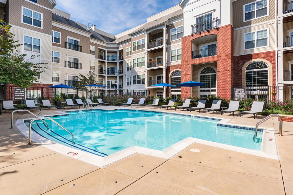 A pool with 3 stairs in, 3 feet at the closest ones. Lots of lounge chairs with umbrellas, and a no lifeguard notice.