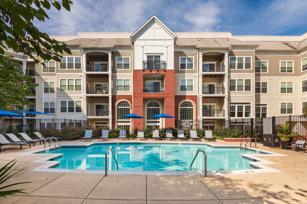 Outdoor pool with lots of umbrellas and lounge chairs, overlooked by Bell Arlington Ridge, a 4 story building.