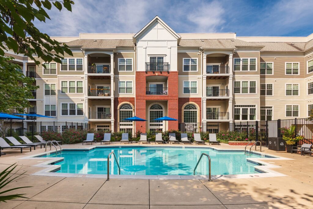 Outdoor pool with lots of umbrellas and lounge chairs, overlooked by Bell Arlington Ridge, a 4 story building.