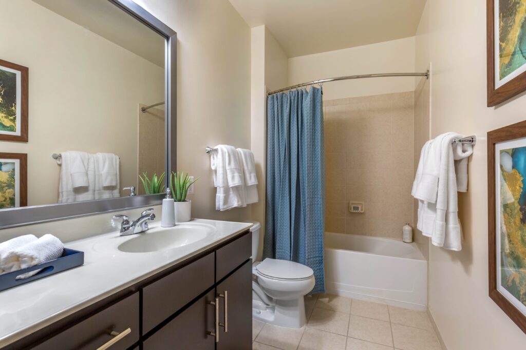 A bathroom with tile floors, tiled shower/tub, curved shower curtain rod, and a large mirror. It is identical to the other bathroom in this model.