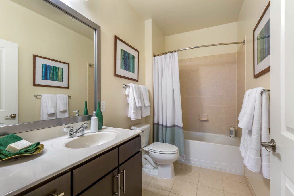 A bathroom with tile floors, tiled shower/tub, curved shower curtain rod, and a large mirror.