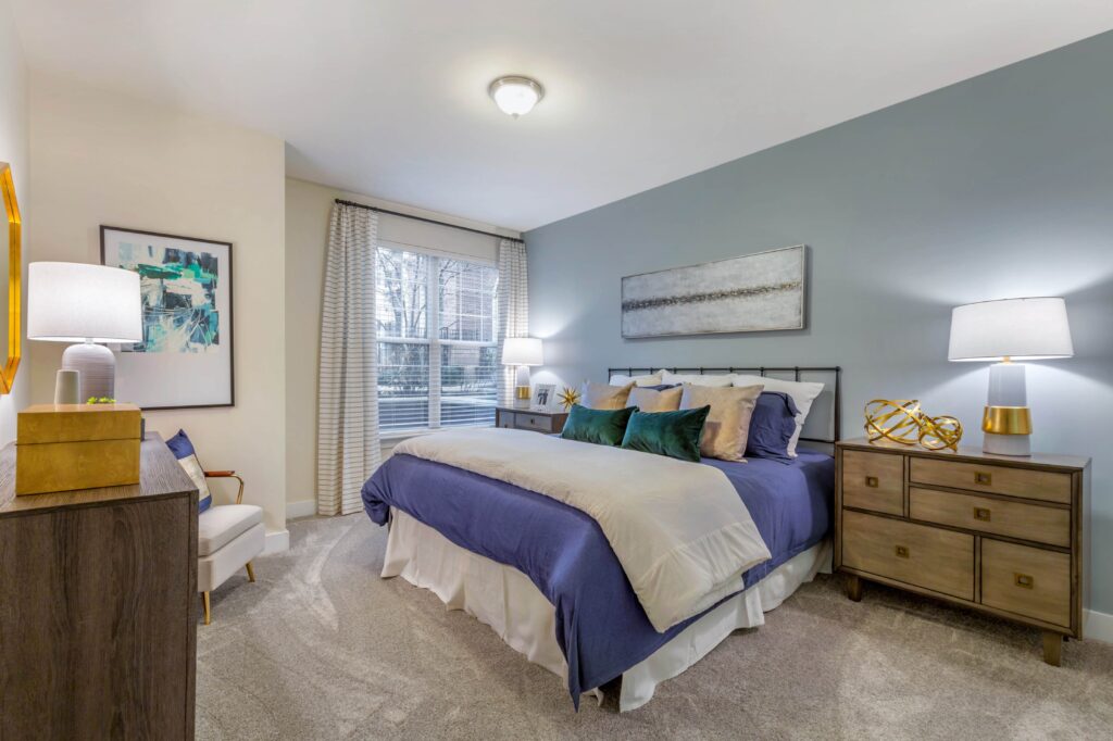 a bedroom with an accent wall, carpet, and a large widow, big enough for a queen bed, two side tables, a dresser and a chair.