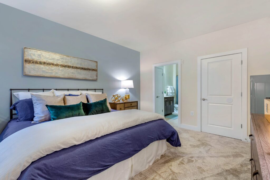 A queen size bedroom with carpet and a blue accent wall, a door opens into a bathroom.