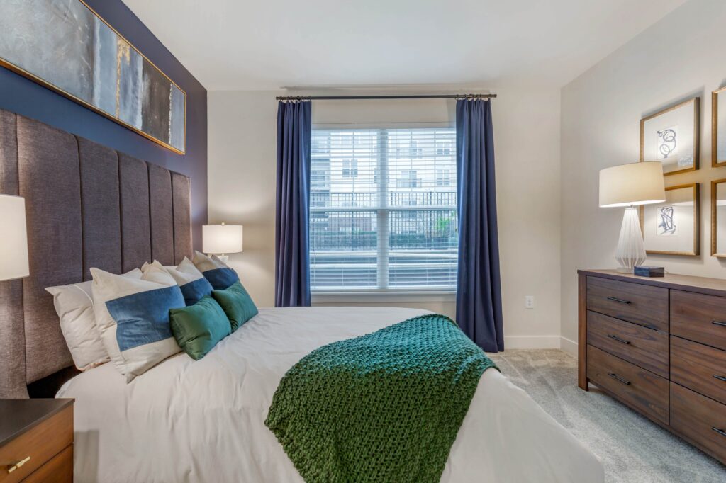 Bedroom with a large window, a dark blue accent wall, and carpet.