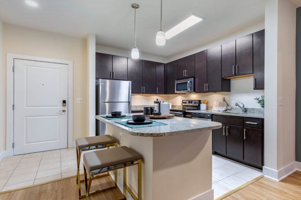 Modern kitchen with island with seating for two, tile floors, ample lighting, stainless steel appliances and lots of counter space.