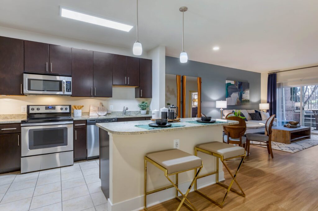 Kitchen and living room open space with island seating for two, room for a dining table, tile kitchen floors, wood look floors, and stainless steel appliances.