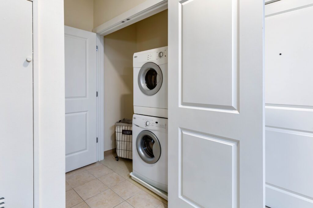Tile floor hallway with double doors that open to reveal stacked washer and dryer and space for a hamper next to it.