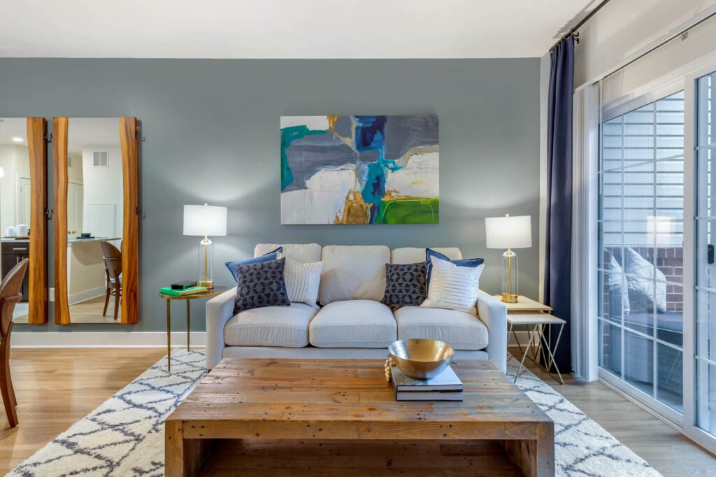 A living room with a blue accent wall and a couch next to big glass window doors that lead to a balcony.